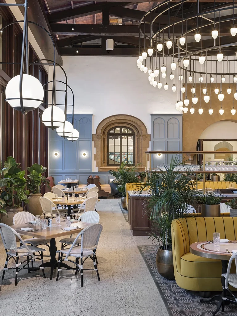 Empty, bright restaurant interior with varied seating, plants, and light fixtures.