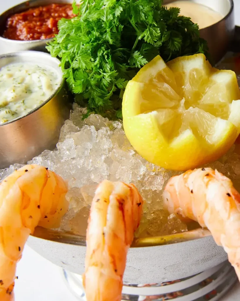 Shrimp cocktail with sauces, lemon, and parsley on crushed ice.