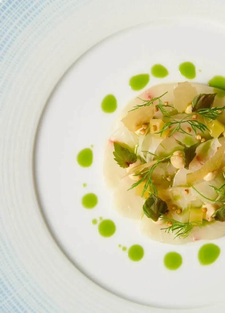 Meticulously plated carpaccio or crudo with herbs and green sauce.