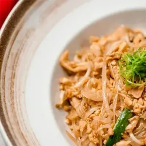 A bowl of Pad Thai-like noodles with peanuts and green garnish.