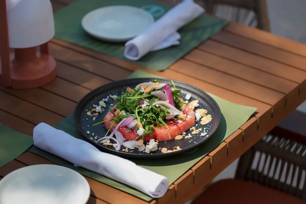 Watermelon salad with arugula, cheese, and almonds on a wooden table.