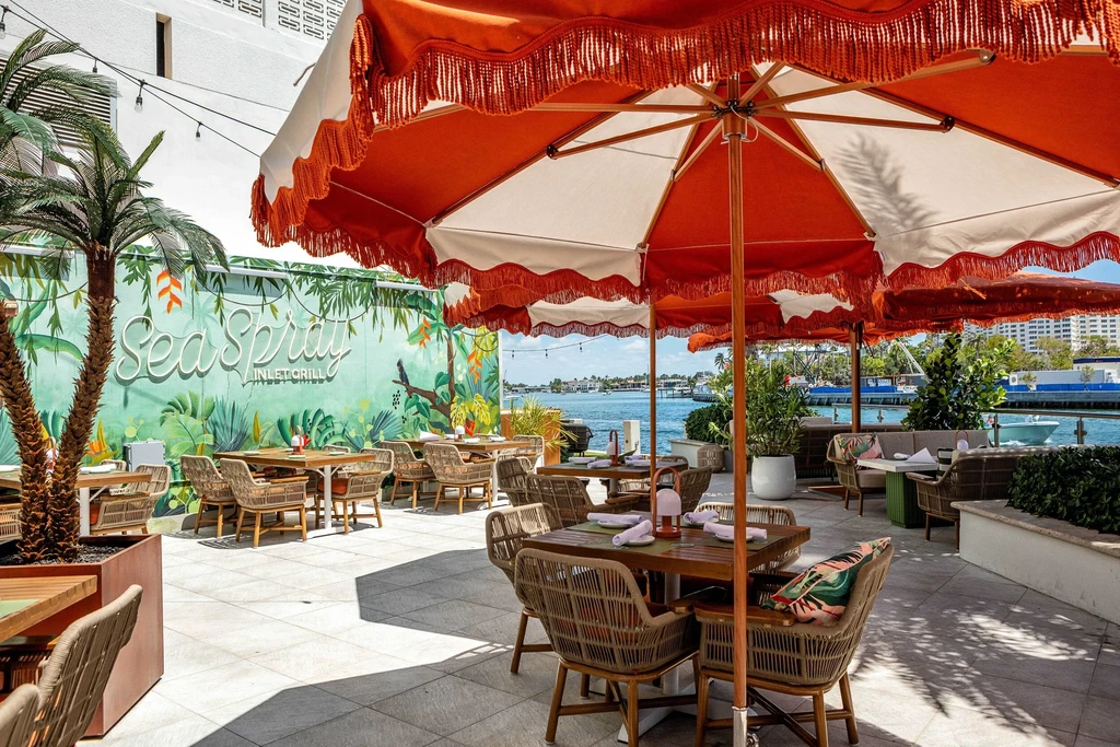 Empty tropical waterfront patio with orange umbrellas and restaurant mural.