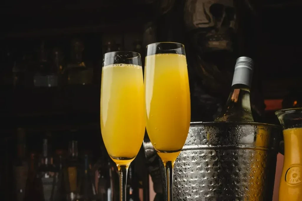 Two mimosas, wine bottle in ice bucket, subtle skull decor, dark background.