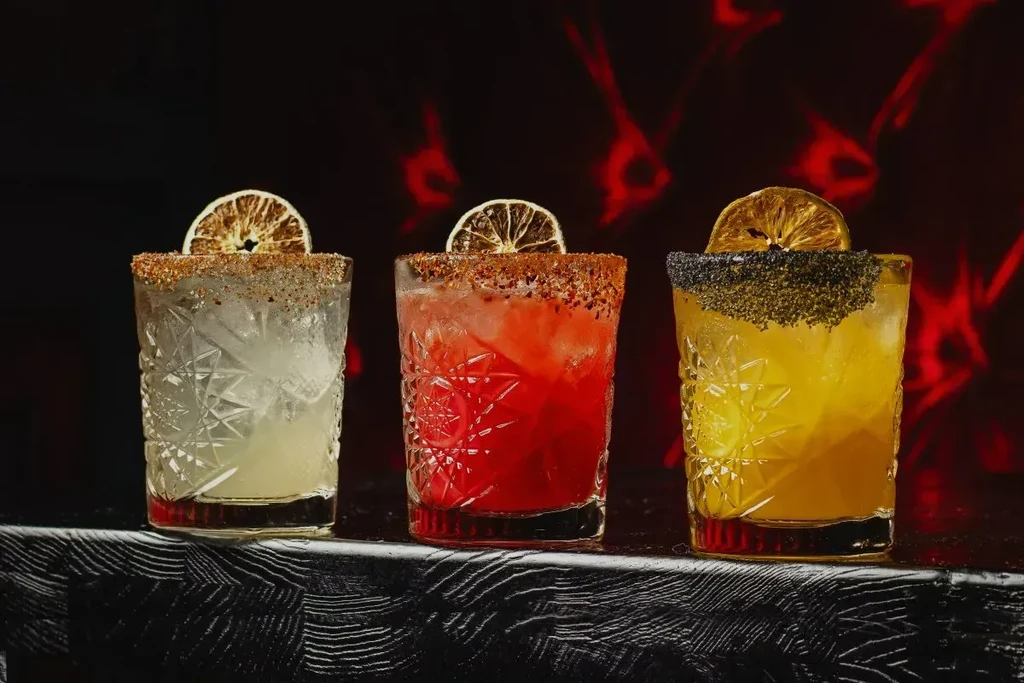 Three colorful cocktails in ornate glasses with spice and dried citrus garnishes.