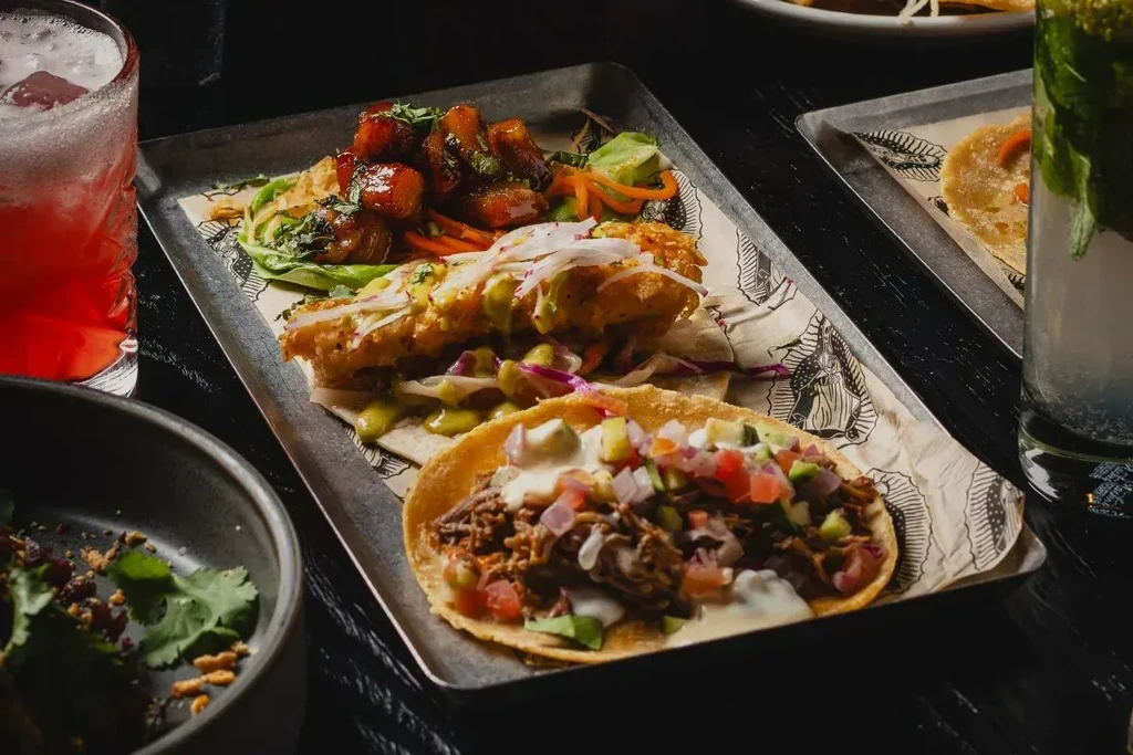 Close-up: Three small dishes and two cocktails on a dark table.