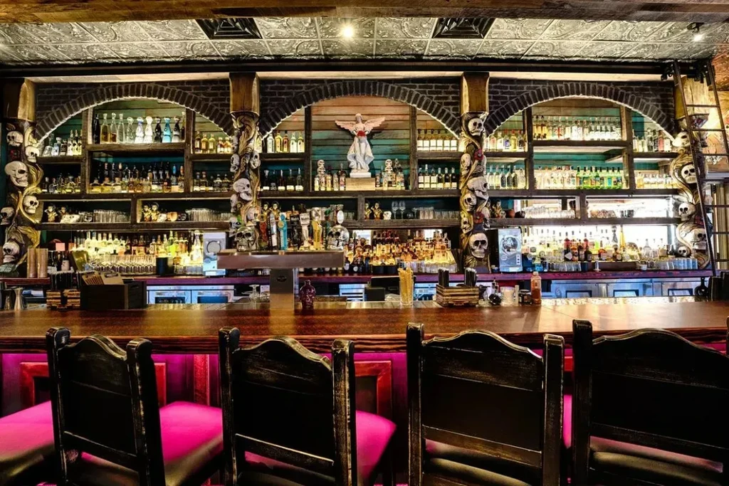 Elaborate bar with skull pillars, angel statue, and bright pink stools.
