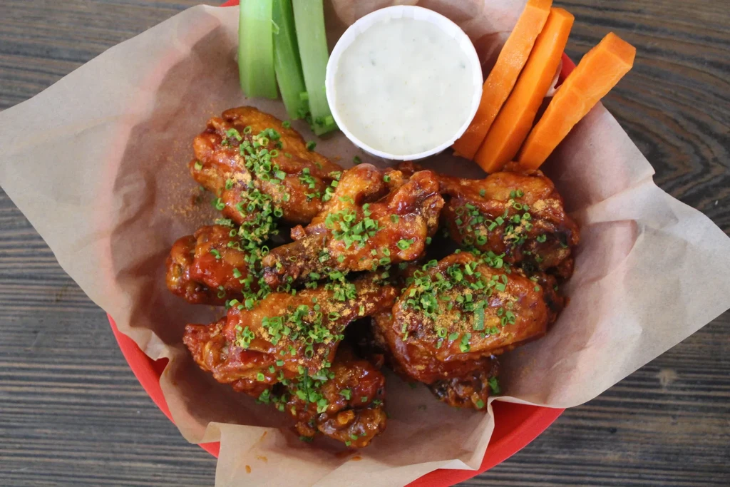 Top-down view of buffalo chicken wings with celery, carrots, and dip.