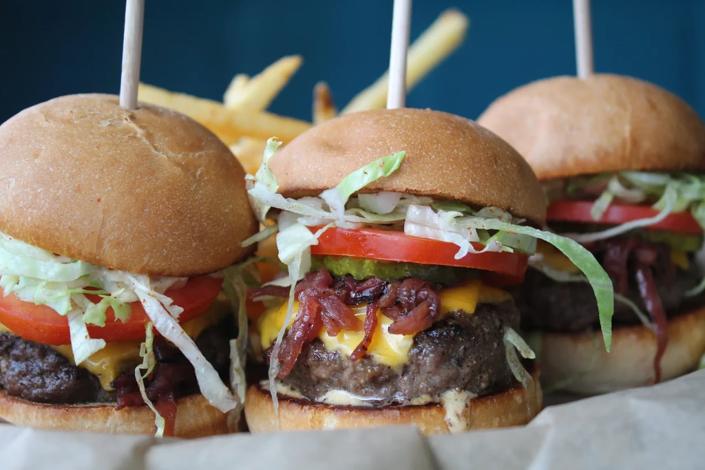 Three cheeseburger sliders with caramelized onions, pickles, and fries.