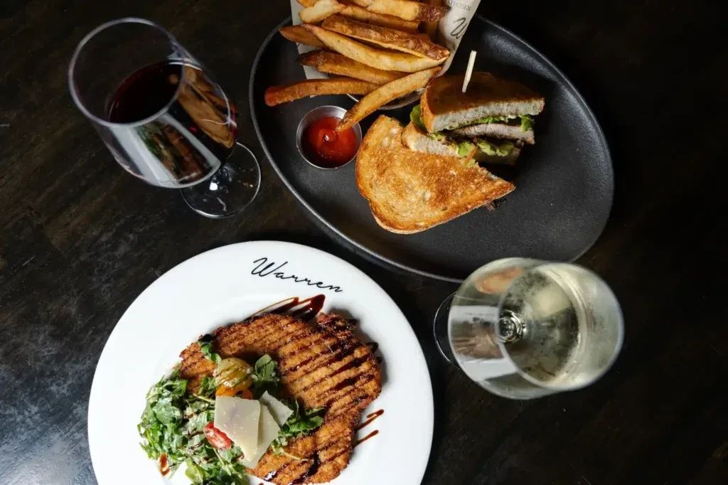 Overhead view: schnitzel, club sandwich, fries, salad, and two wines.