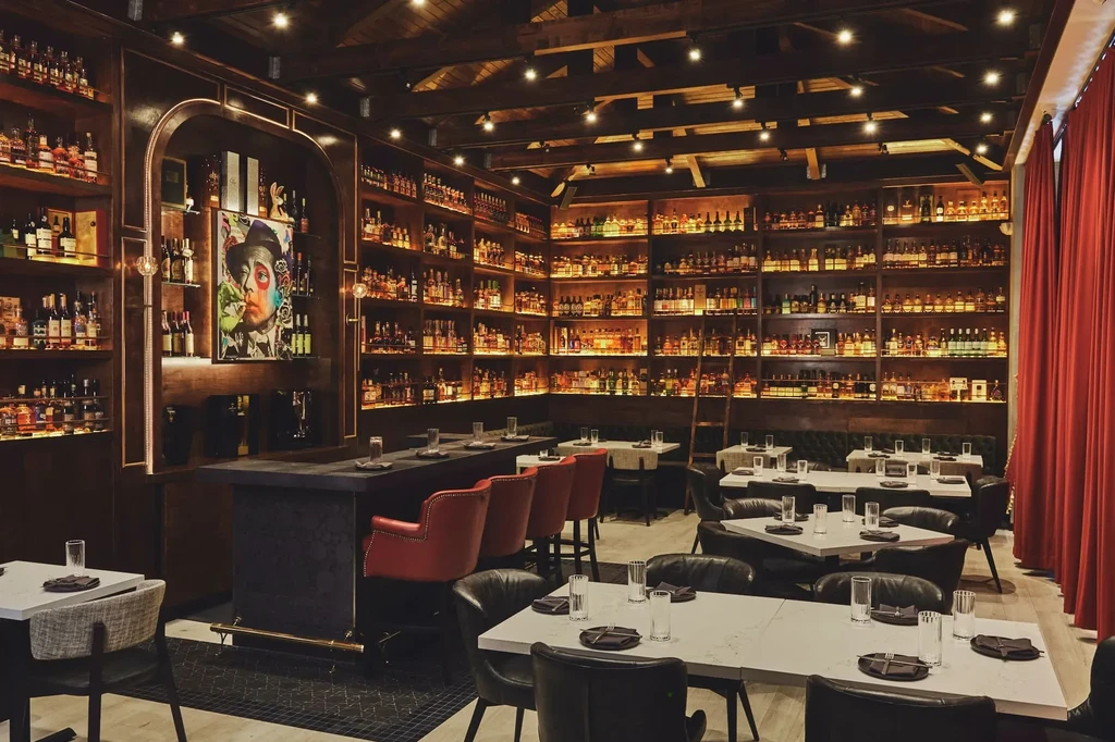 Upscale restaurant interior with illuminated spirit shelves, bar, and dining area.