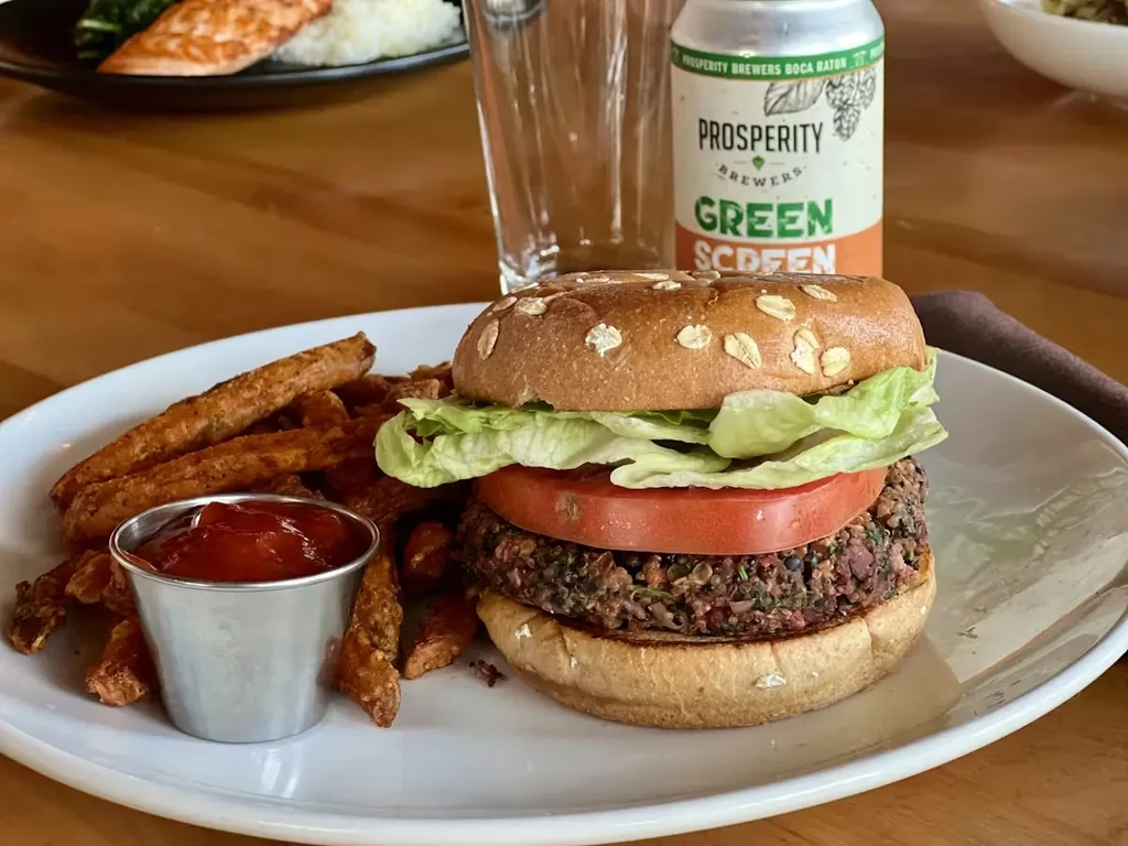 Plant-based burger, sweet potato fries, ketchup, beer on a wooden table.