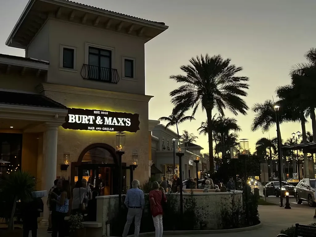 Exterior of Burt & Max's Bar and Grille at dusk, with people.