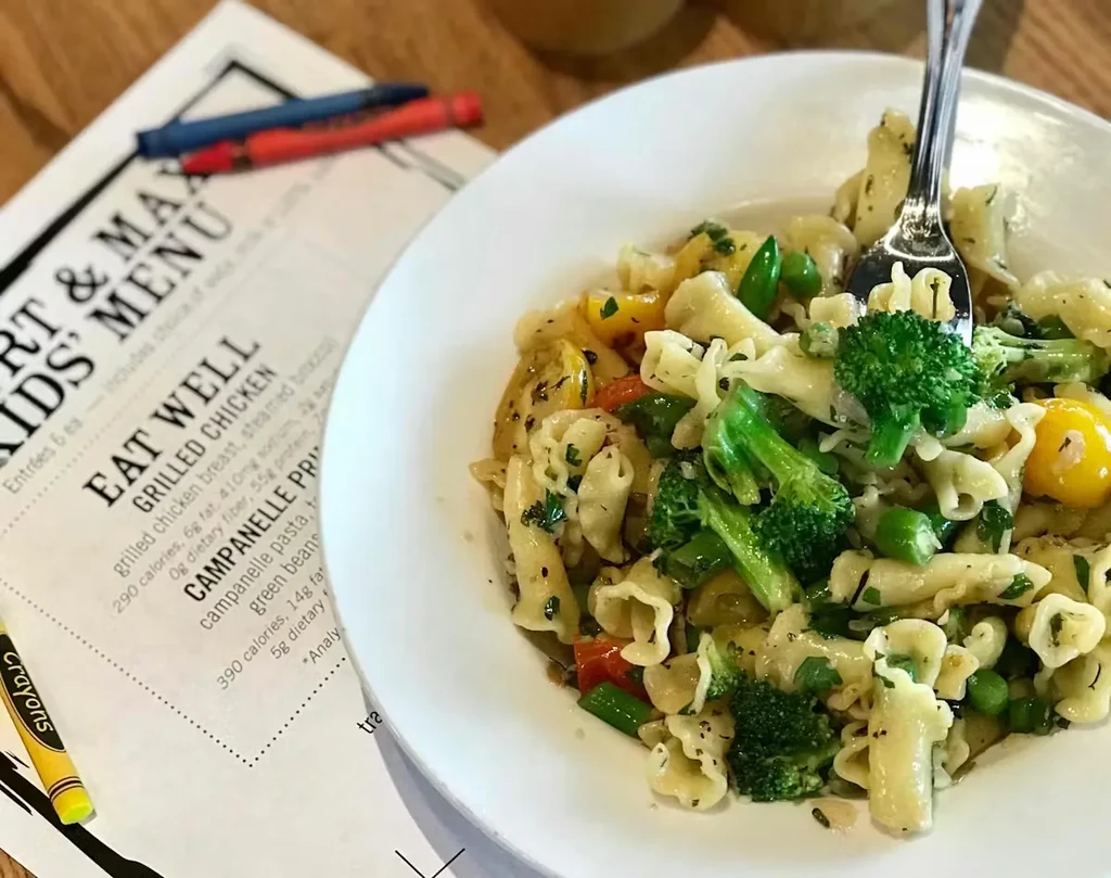 Bowl of campanelle pasta, mixed vegetables, fork, kids' menu.