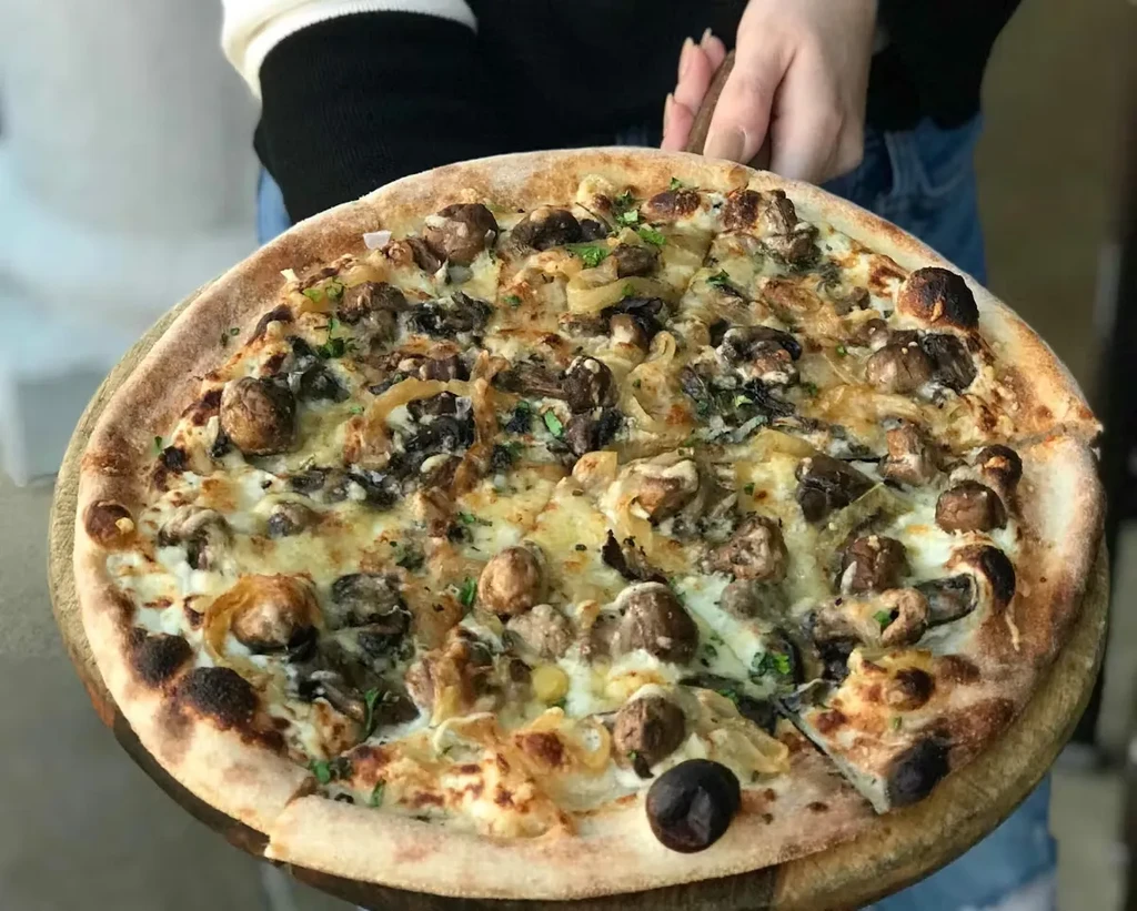 Mushroom and onion pizza on a wooden paddle, one slice removed.