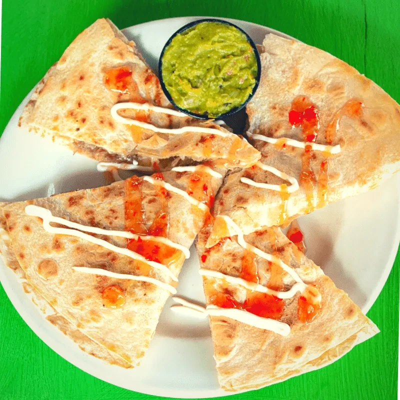 Quesadilla wedges with crema, chili sauce, and guacamole on a green background.