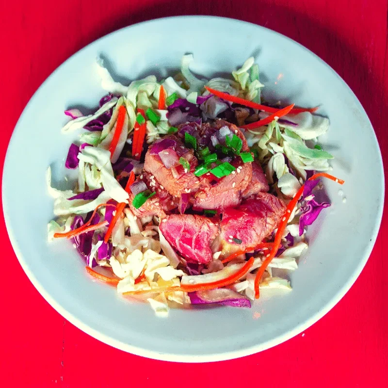 Plated seared meat with shredded cabbage, carrots, and sesame seeds.