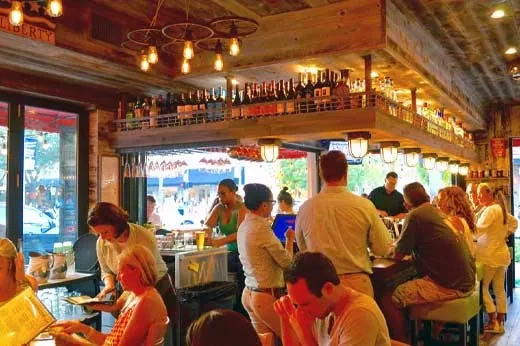Lively rustic-industrial bar and restaurant interior with many patrons.
