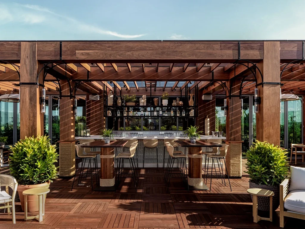 Rooftop bar area with wooden pergola, seating, and green plants.
