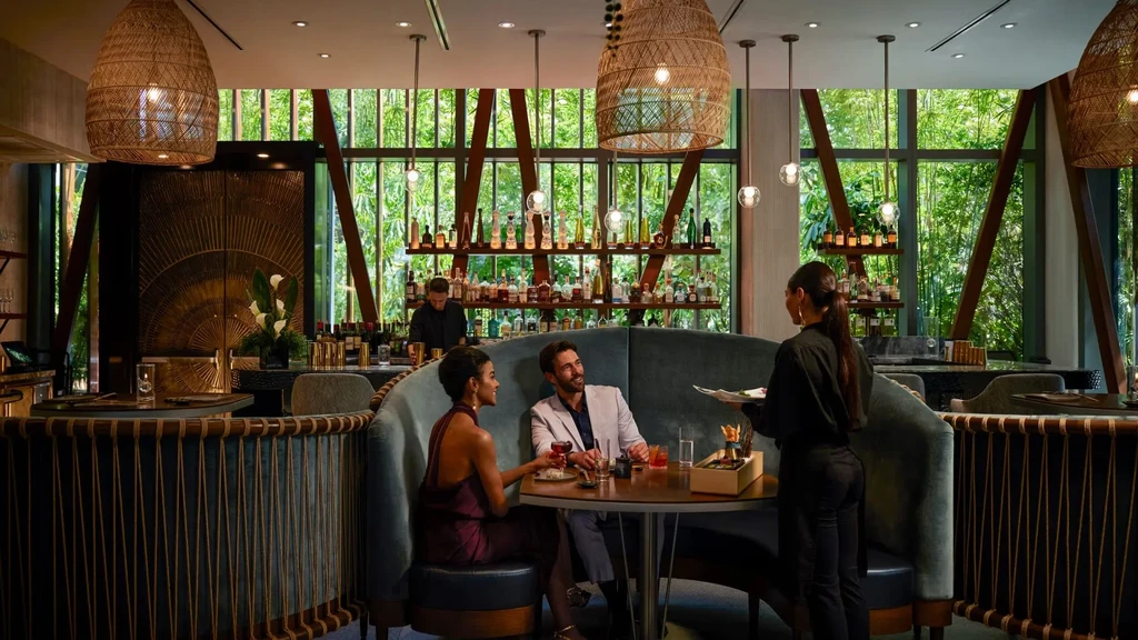 Couple served drinks in a teal booth at an upscale, nature-inspired restaurant.