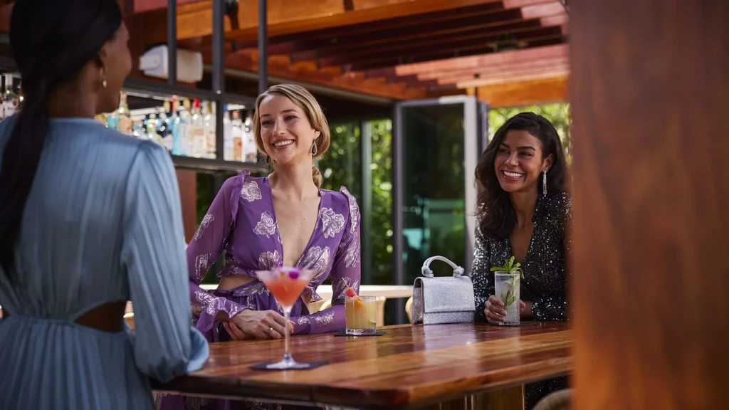 Three women socialize with cocktails at an upscale bar.