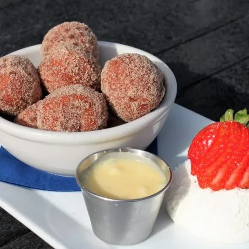 Bowl of cinnamon-sugar donut holes, dipping sauce, and strawberry cream.