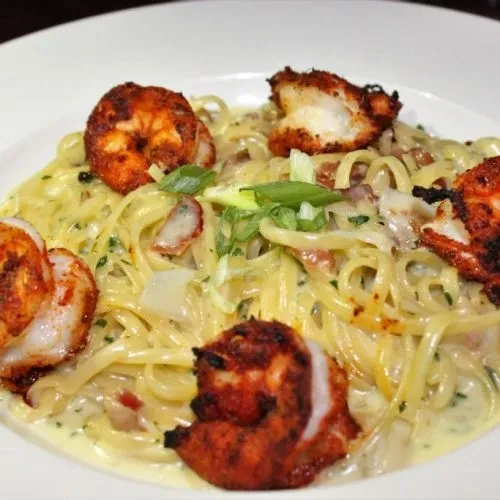 Top-down view of creamy pasta with seasoned seafood and green onions.