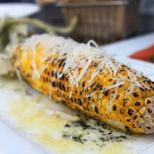 Grilled corn with char marks, cheese, and melted herb butter.