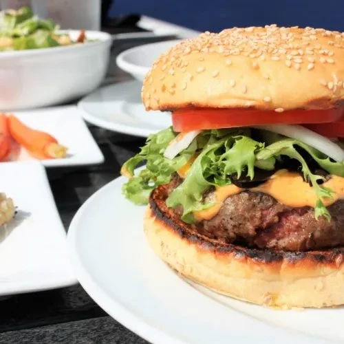Close-up: large hamburger with sesame bun, patty, cheese, lettuce, tomato.