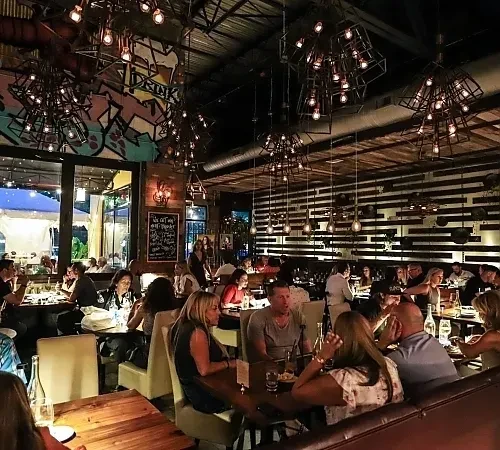 Bustling modern industrial restaurant at night with warm lighting and patrons.