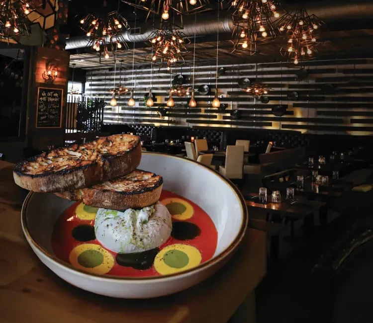 Dish of creamy cheese, tomato, and grilled bread in a modern restaurant.