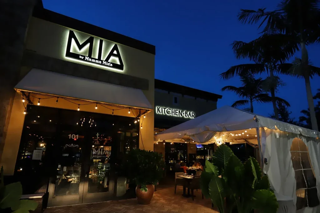 Brightly lit MIA by Mamma Mia's restaurant exterior and outdoor dining at night.