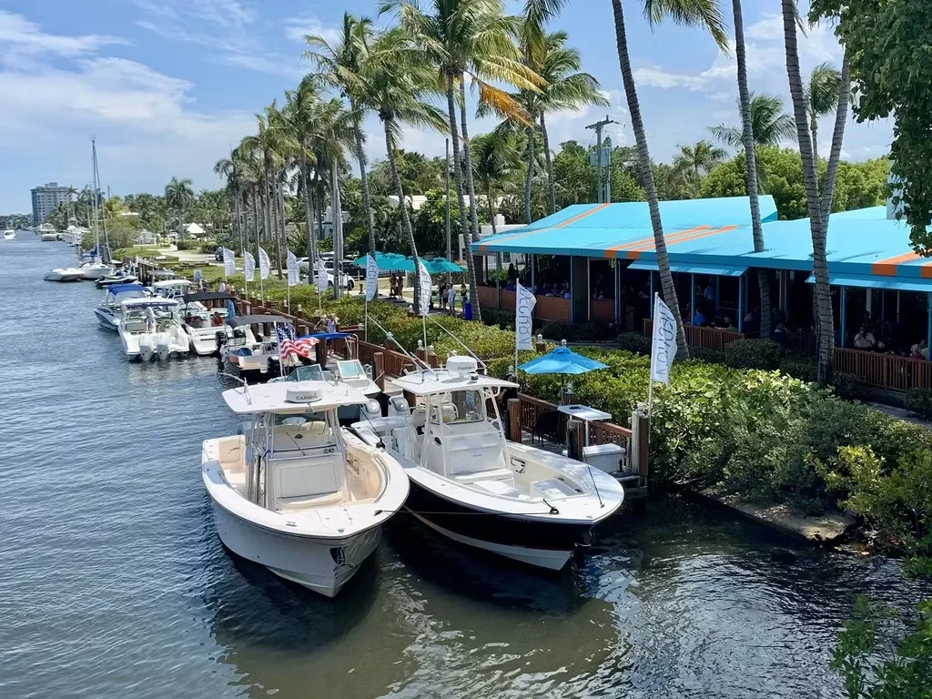 Waterfront restaurant with striped blue roof, boats, and palm trees.