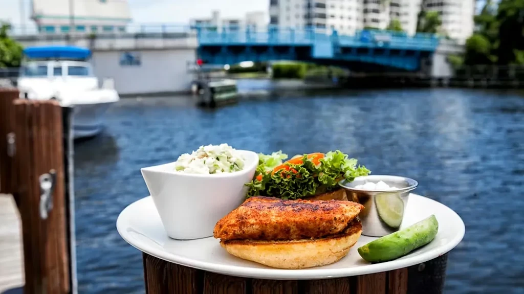 Fish or chicken sandwich, coleslaw, pickle, by water and drawbridge.