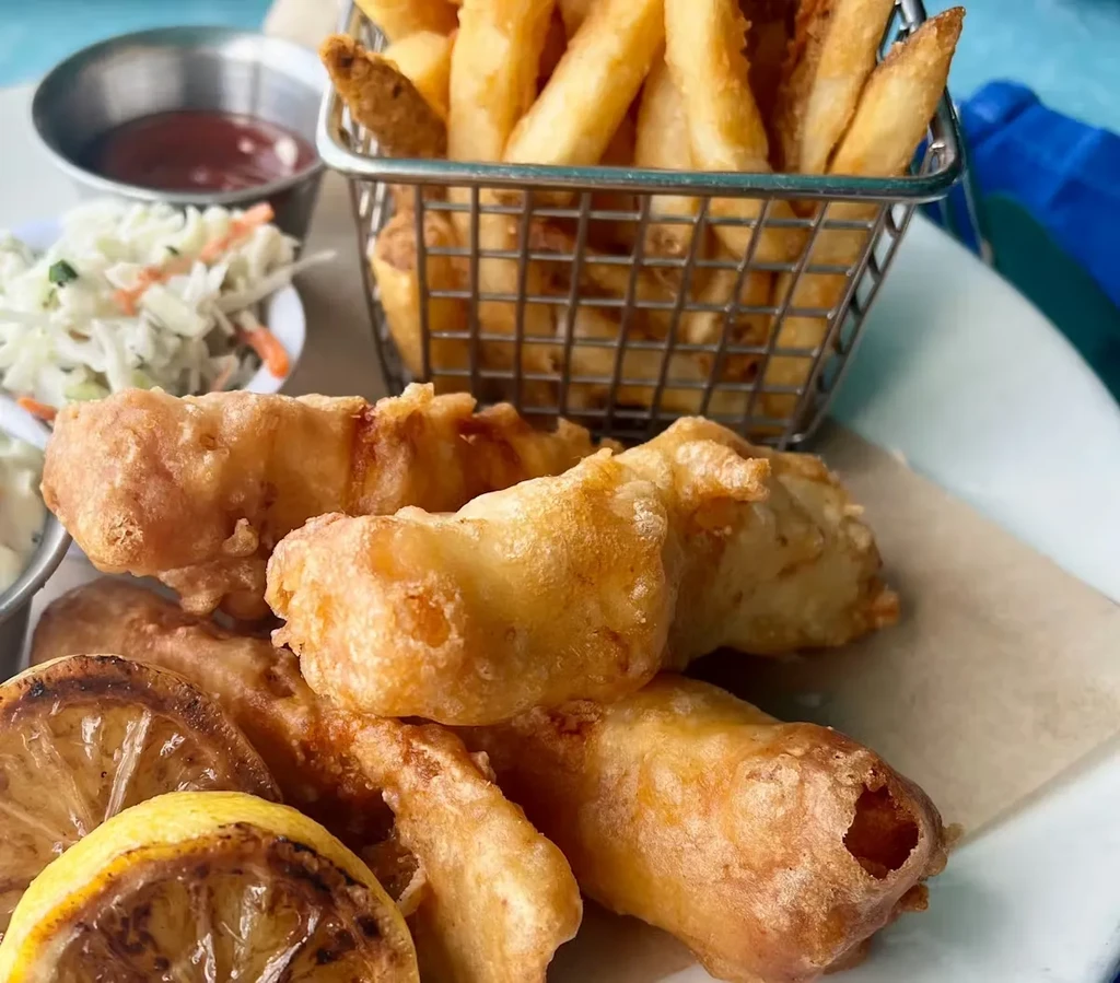 Crispy fried fish and chips meal with sauces, coleslaw, and grilled lemon.