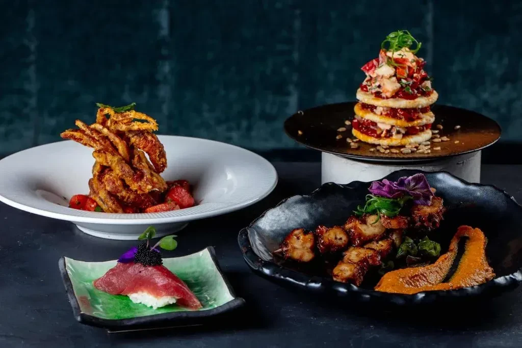 Gourmet spread of four artfully arranged dishes with dramatic lighting.