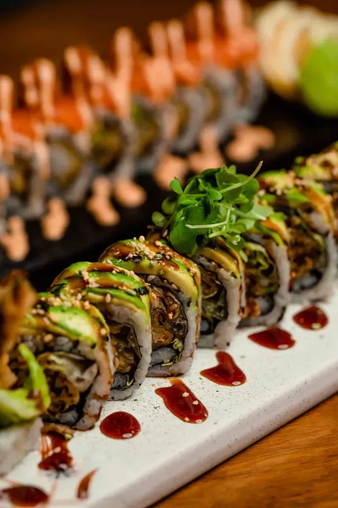 Sushi rolls topped with avocado, dark sauce, sesame seeds, and microgreens.