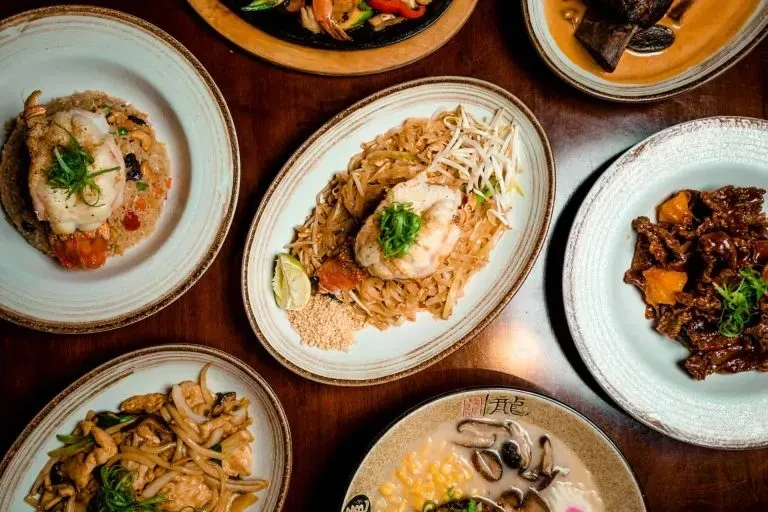 Overhead view of a wooden table with various plated Asian dishes.