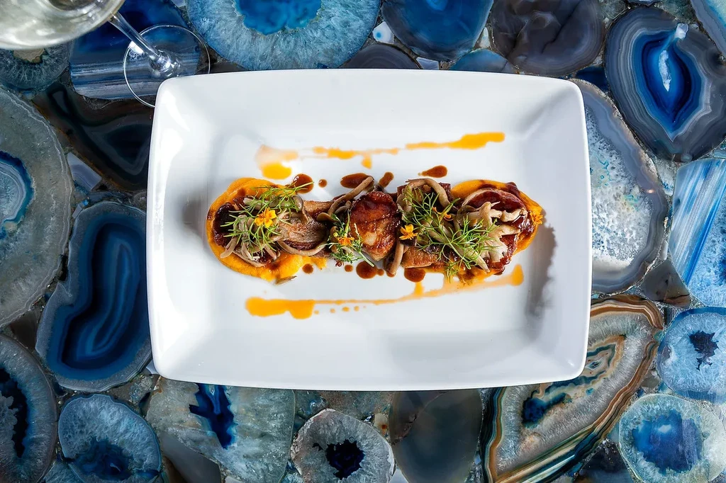 Overhead view: scallops, mushrooms, orange puree, microgreens, flowers on agate.