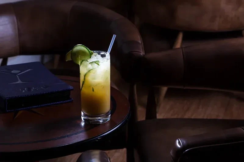Layered cocktail with cucumber and straw on table next to menu.