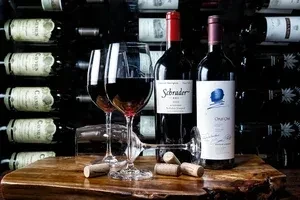 Still life of red wine glasses, bottles, corks, against a wine rack.