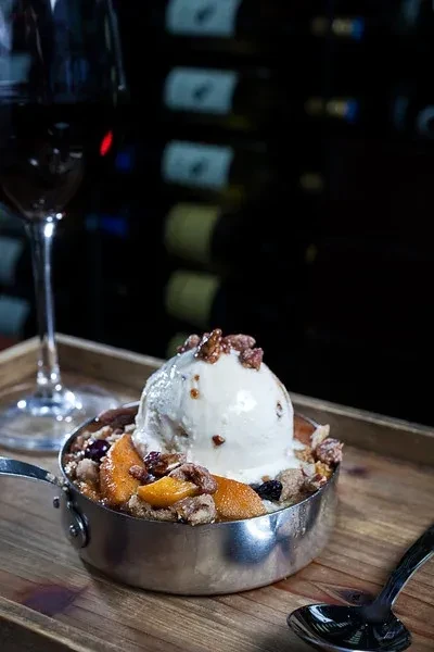 Warm fruit crumble with melting ice cream, nuts, and red wine.