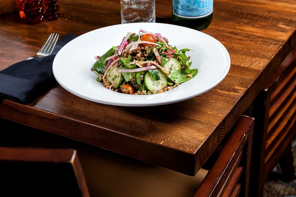 Gourmet salad in white bowl with vegetables, grains, and sparkling water.