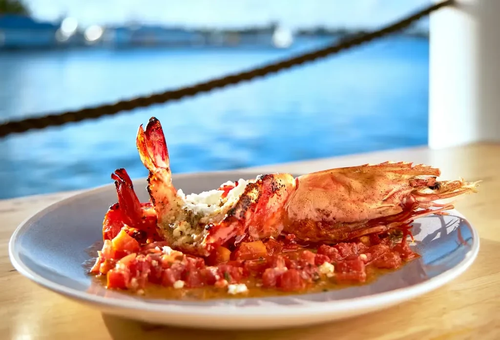 Plate of cooked prawns, tomato sauce, cheese, herbs, overlooking blue water.