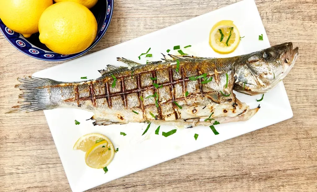 Whole grilled fish with herbs and lemon on a white plate.