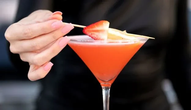 Hand garnishing red-orange cocktail with strawberry and citrus.