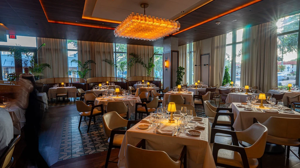 Upscale restaurant dining room with set tables, chandelier, and natural light.