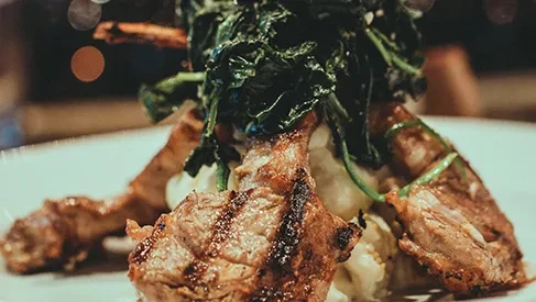Artfully plated grilled meat, mashed potatoes, and sautéed greens.