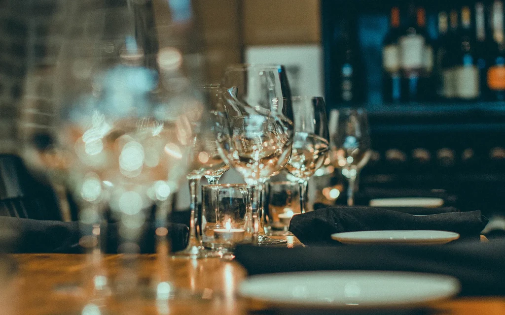 Warmly lit restaurant table setting with glasses, candles, and napkins.