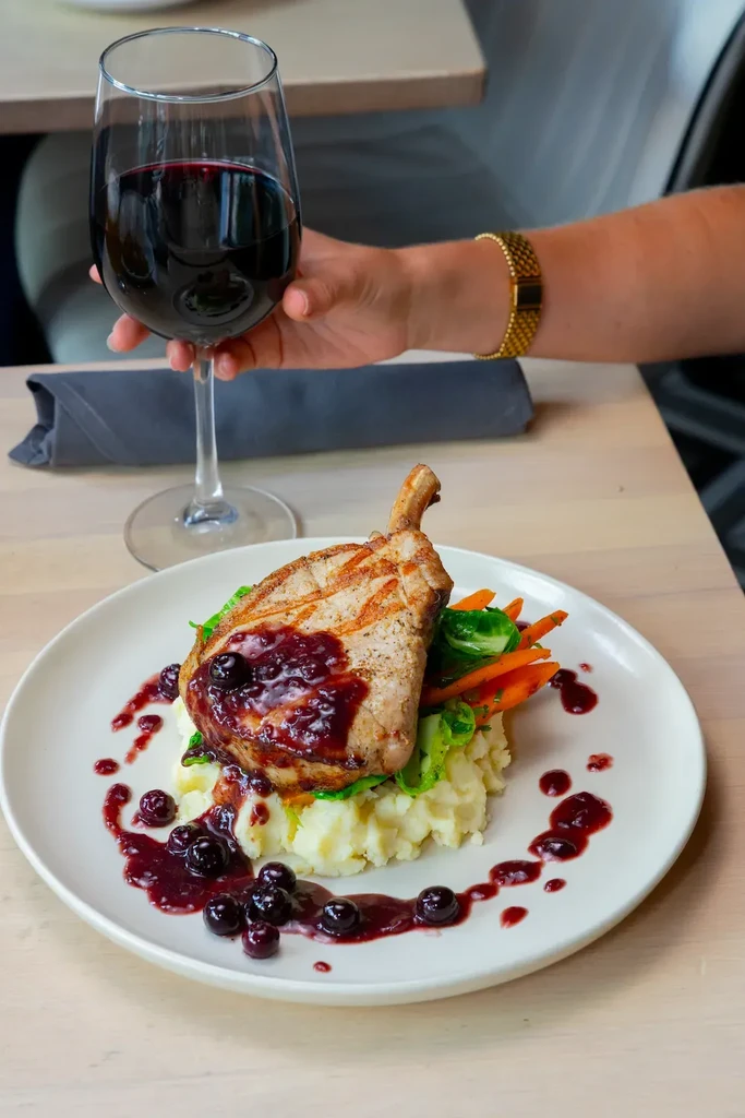 Grilled pork chop with berry sauce, mashed potatoes, vegetables, and red wine.