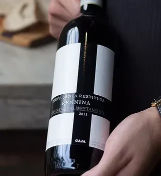 Two hands holding a Gaja Brunello di Montalcino 2011 wine bottle.